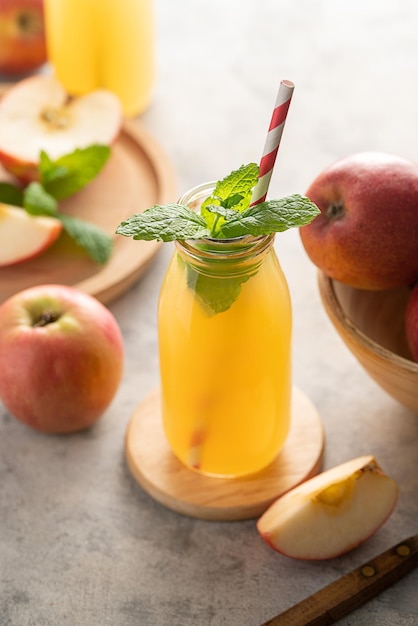 Jugo de manzana en botellas de vidrio con menta fresca y fondo de madera de manzanas rojas