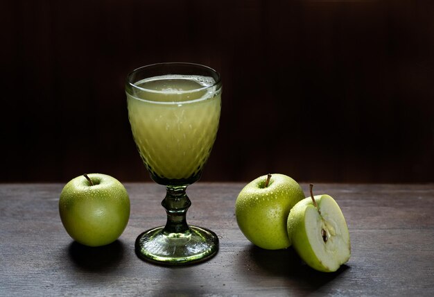 Jugo de manzana fresco en un hermoso vaso con manzanas verdes cerca y fondo negro Foto de alta calidad