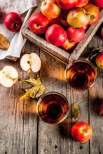 Foto jugo de manzana de granja orgánica fresca en vasos con manzanas rojas crudas enteras y en rodajas, en la vieja mesa de madera rústica, vista superior de copyspace
