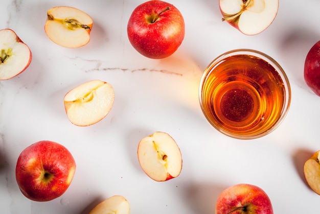 Jugo de manzana de granja orgánica fresca en vasos con manzanas rojas enteras crudas y en rodajas, en la mesa de mármol blanco, vista superior de copyspace