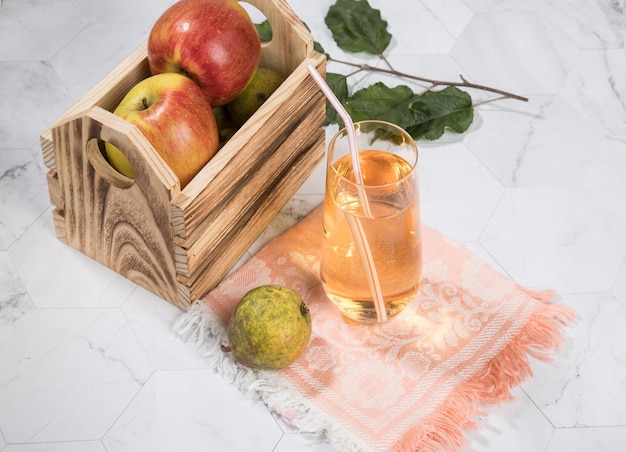 Jugo de manzana y pera en un vaso de vidrio manzanas en una caja de madera sobre un fondo claro