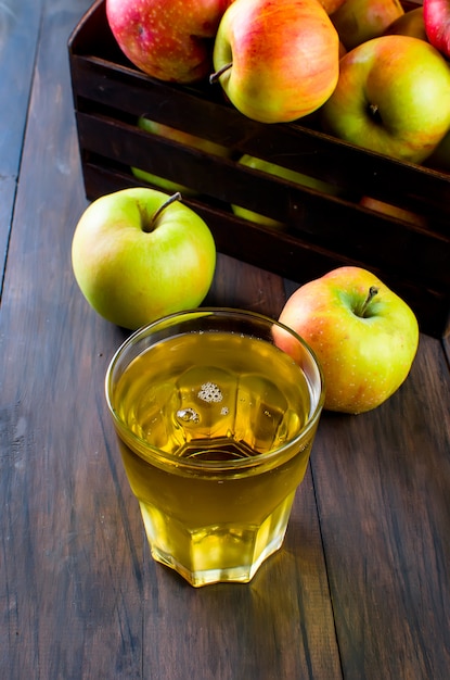 Jugo de manzana en un vaso y manzanas maduras en una mesa de madera