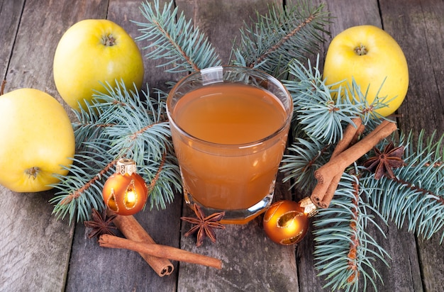 Foto jugo de manzana en vidrio, manzanas, especias y abeto en el fondo de madera vieja