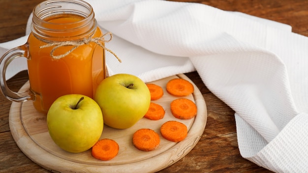 Jugo de manzana y zanahoria en vidrio, verduras frescas y frutas sobre fondo de madera. Estilo rústico. Bebida casera con vitaminas