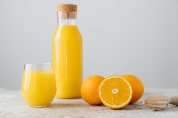 Jugo de naranja cítrica en botella de vidrio, naranjas frescas y exprimidor