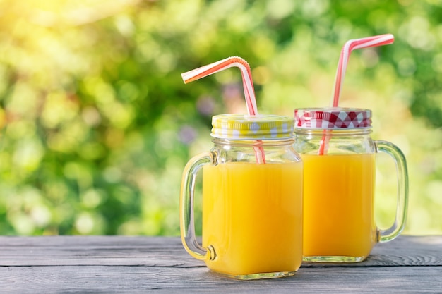 Jugo de naranja en frascos con las pajitas en la mesa de madera