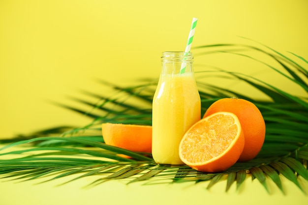 Jugo de naranja fresco en frasco de vidrio. Batido de naranja fresco en botella sobre hojas de palma verde