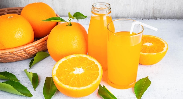 El jugo de naranja fresco y la fruta de naranja están en una canasta sobre un fondo de madera blanca