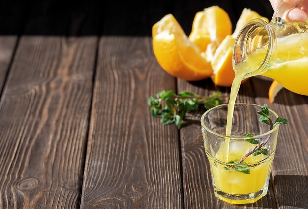 El jugo de naranja fresco se vierte en un vaso con hielo y hojas de menta