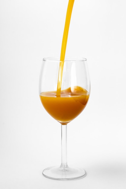 El jugo de naranja fresco se vierte en un vaso sobre un fondo blanco.