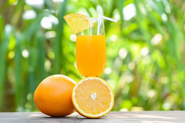 Jugo de naranja con fruta de naranja de pieza en vidrio con fondo verde de verano de naturaleza