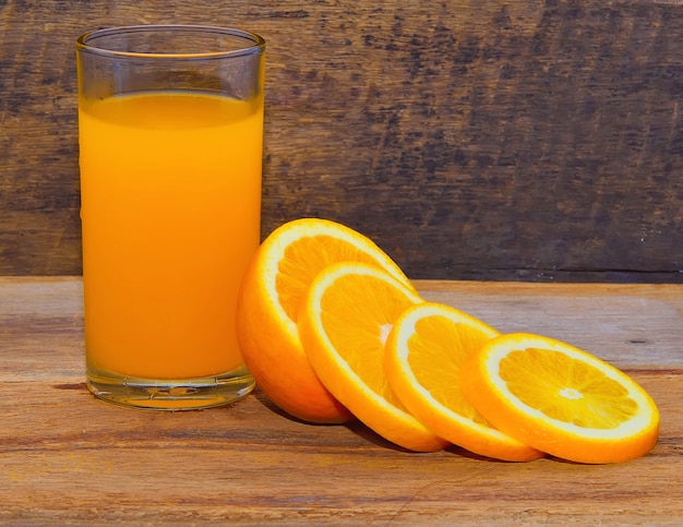 Foto jugo de naranja y rodajas de naranja sobre una mesa de madera.