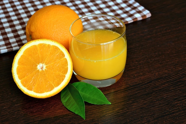 jugo de naranja en vaso con fruta naranja sobre fondo de madera oscura