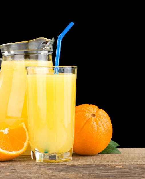 Jugo de naranja en vaso y jarra aislado sobre fondo negro