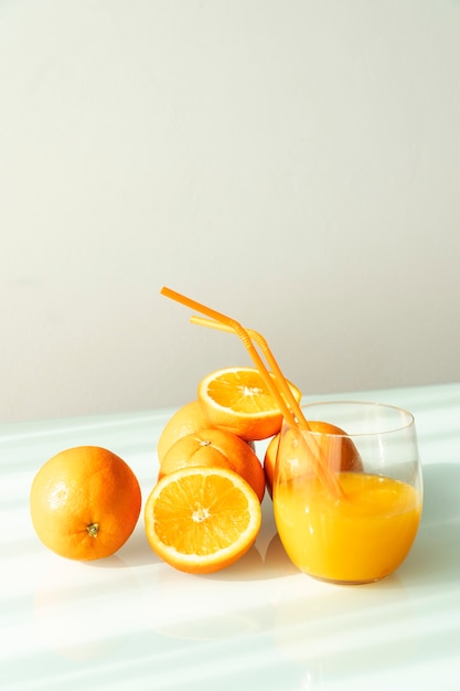 Jugo de naranja en un vaso rodeado de naranjas naturales con un fondo blanco de luz solar natural