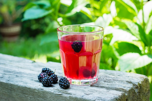 Jugo o limonada de Blackberry en vidrio en fondo de madera de la tabla. Fondo de hoja verde natural