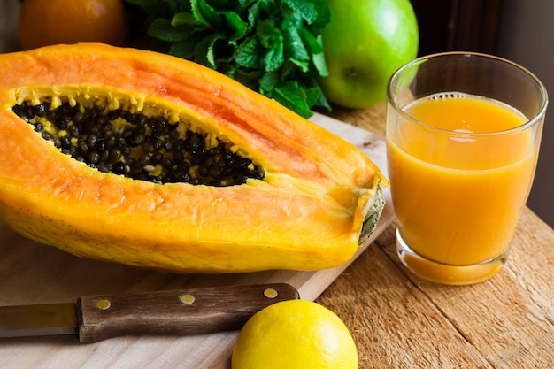 Jugo de papaya recién prensado en vidrio, fruta madura a la mitad en tabla para cortar madera