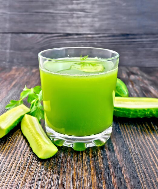 Jugo de pepino en un vaso, verduras y perejil sobre un fondo de tablero de madera