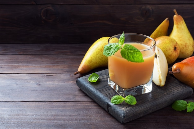 Jugo de pera natural en una taza de vidrio. Jugosas peras maduras de conferencias y hojas de menta. Copie el espacio Fondo de madera rústica oscura.