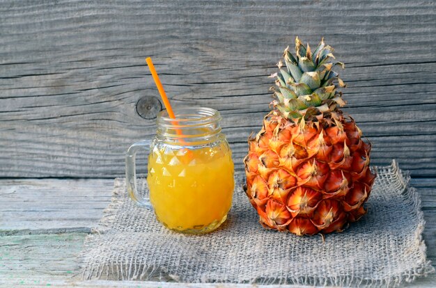 Jugo de piña recién exprimido en una taza de vidrio con pajita y fruta madura de ananas en la mesa de madera vieja. Concepto de comida sana, dieta o comida vegana.