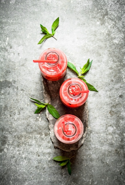 Jugo de sandía en botellas con hojas de menta. Sobre la mesa de piedra.