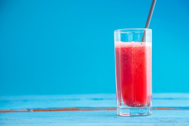 Jugo de sandía exprimido en un vaso transparente sobre un fondo de madera azul