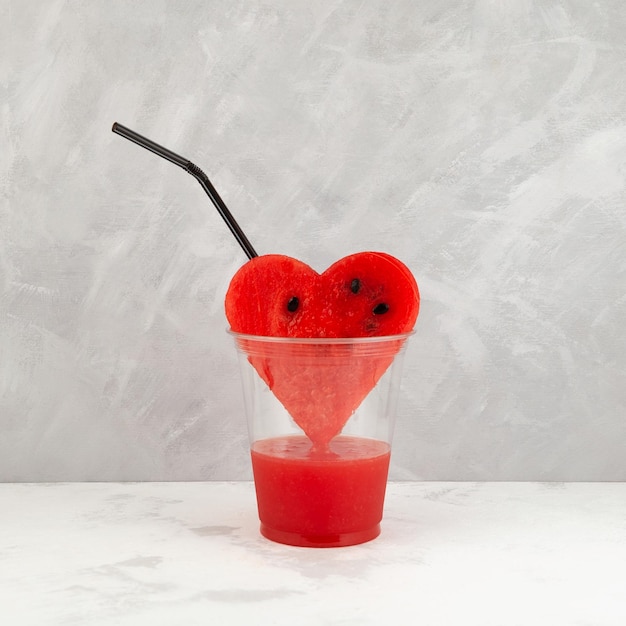 Foto el jugo de sandía gotea en un vaso de plástico desechable de un trozo de pulpa en forma de corazón