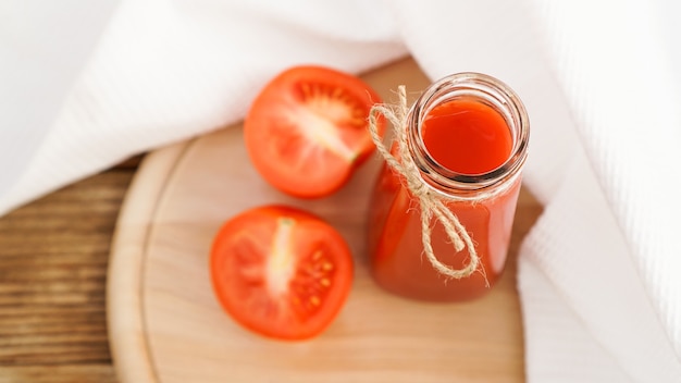 Jugo de tomate en botella de vidrio y tomates frescos sobre tabla de cortar de madera