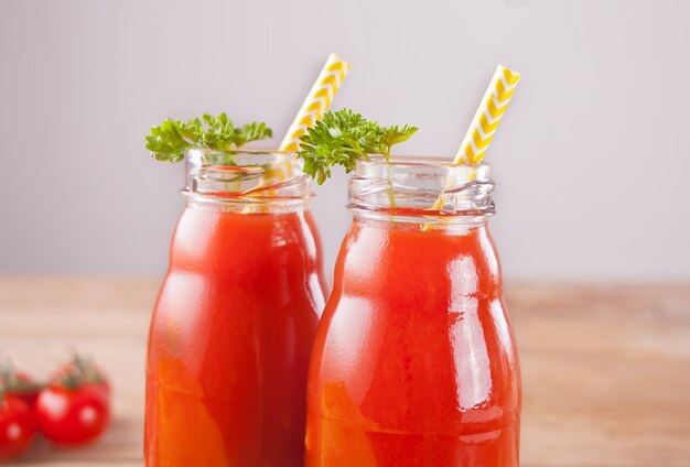 Jugo de tomate en botellas con perejil y sal en la mesa de madera