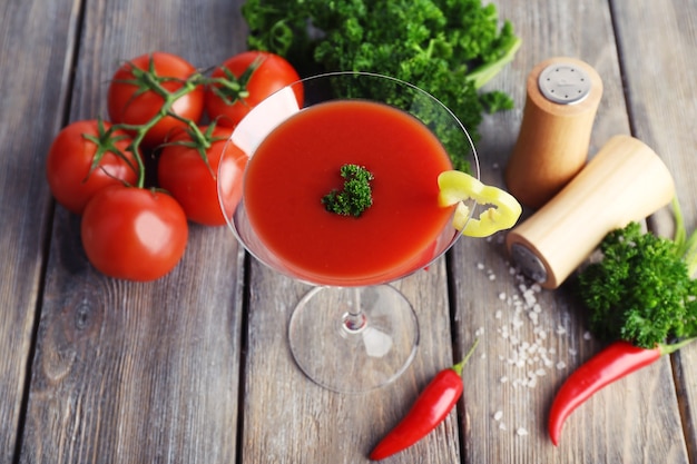 Jugo de tomate en copa y verduras frescas sobre fondo de madera