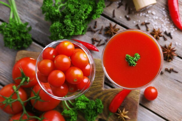 Jugo de tomate en copa y verduras frescas en tabla de cortar sobre fondo de madera