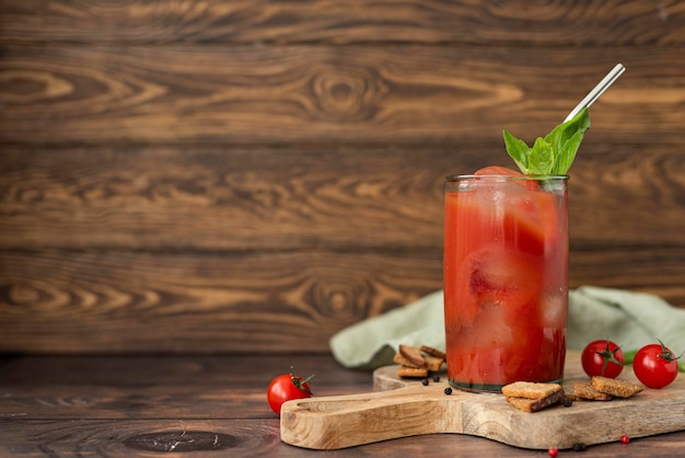 Jugo de tomate con especias, albahaca y picatostes en un vaso sobre una mesa de madera