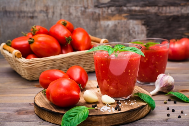 Jugo de tomate fresco con hojas de albahaca en vasos y tomates en una mesa de madera