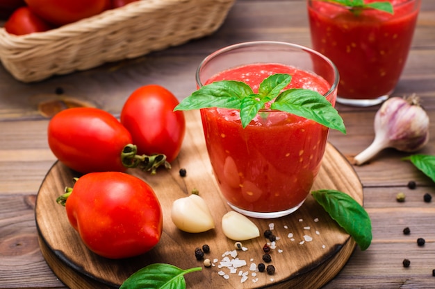 Jugo de tomate fresco con hojas de albahaca en vasos y tomates en una mesa de madera