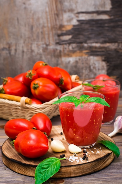 Jugo de tomate fresco con hojas de albahaca en vasos y tomates en una mesa de madera