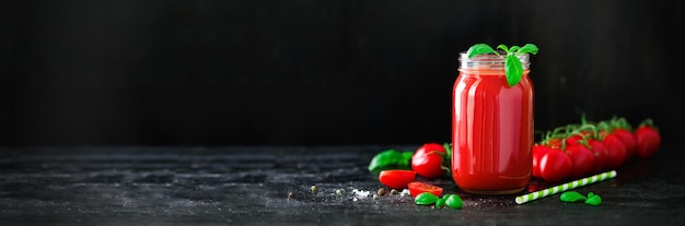 Jugo de tomate fresco orgánico en un frasco de vidrio albahaca cereza sal pimienta y paja sobre fondo negro oscuro Concepto de dieta y alimentación limpia Espacio de copia