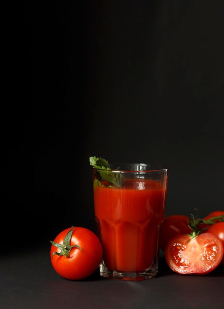 Jugo de tomate fresco en un vaso con tomates sobre un fondo oscuro Bebida de tomate vegetal para una dieta saludable en el fondo