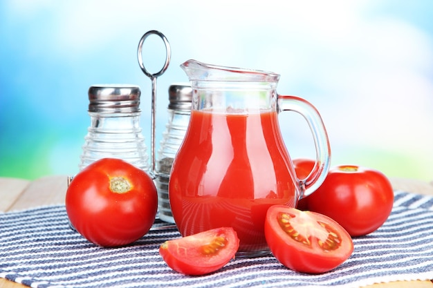 Jugo de tomate en una jarra de vidrio en una mesa de madera sobre un fondo brillante