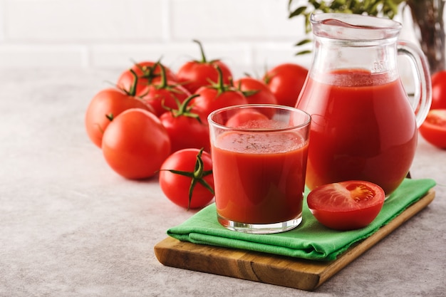 Jugo de tomate sabroso en un vaso con tomates rojos maduros.