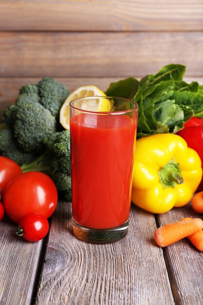 Jugo de tomate en vaso y verduras frescas en una mesa de madera con fondo de pared de madera