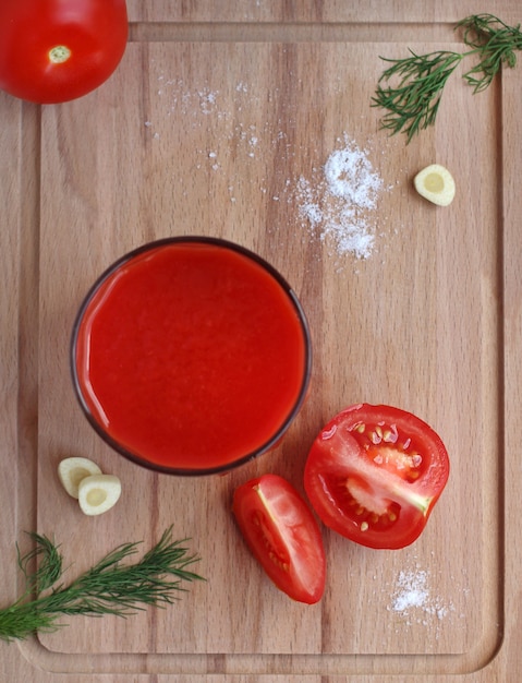 Jugo de tomate en un vaso de vidrio con tomates, sal, ajo y hierbas sobre una tabla de madera