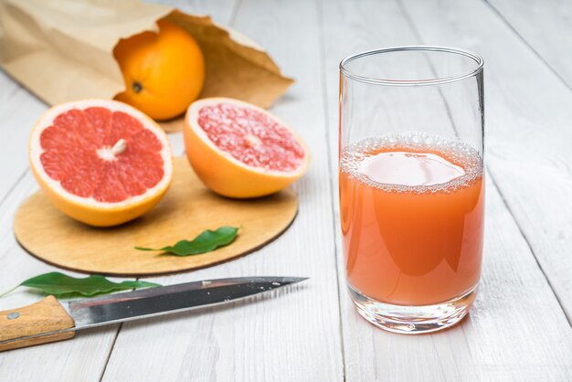 Jugo de toronja en un vaso sobre una mesa de madera naranjas recién cortadas en el fondo