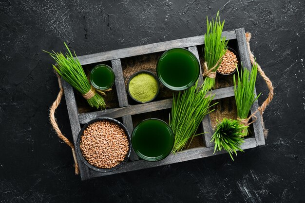 El jugo del trigo verde brotado y los granos de trigo Sobre un fondo negro Micro Green Alimentos saludables Vista superior Espacio libre para su texto