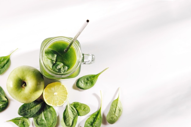 Jugo de vegetales verdes saludables con espinacas y frutas y verduras verdes en el cuadro blanco.