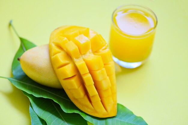 Jugo de verano de mango en vidrio con una rodaja de mango dulce y madura sobre hojas verdes de fruta tropical de árbol