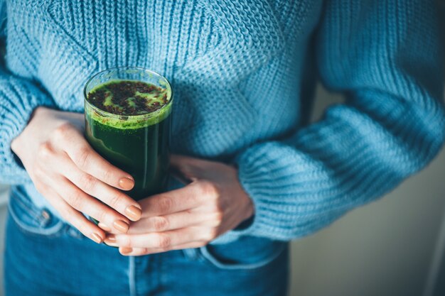 jugo verde fresco sostenido por mujer en suéter de punto