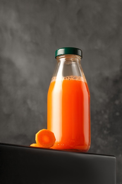 Jugo de zanahoria en botella de vidrio Jugo recién exprimido sobre fondo oscuro Maqueta de empaque y menú
