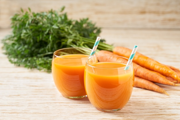 Jugo de zanahoria fresca en vasos sobre una mesa de madera blanca, enfoque selectivo. Dieta de desintoxicación saludable.