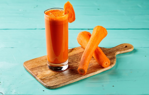 Jugo de zanahoria fresco con zanahorias crudas servido en un vaso aislado en la vista lateral de la tabla de cortar jugo de fruta saludable