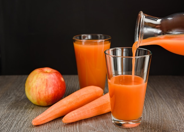 El jugo de zanahoria y manzana se vierte de la botella en un vaso